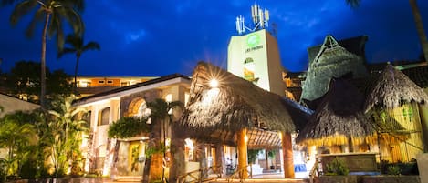 A hotel with a thatched-roof structure, palm trees, and a prominent tower with signage.