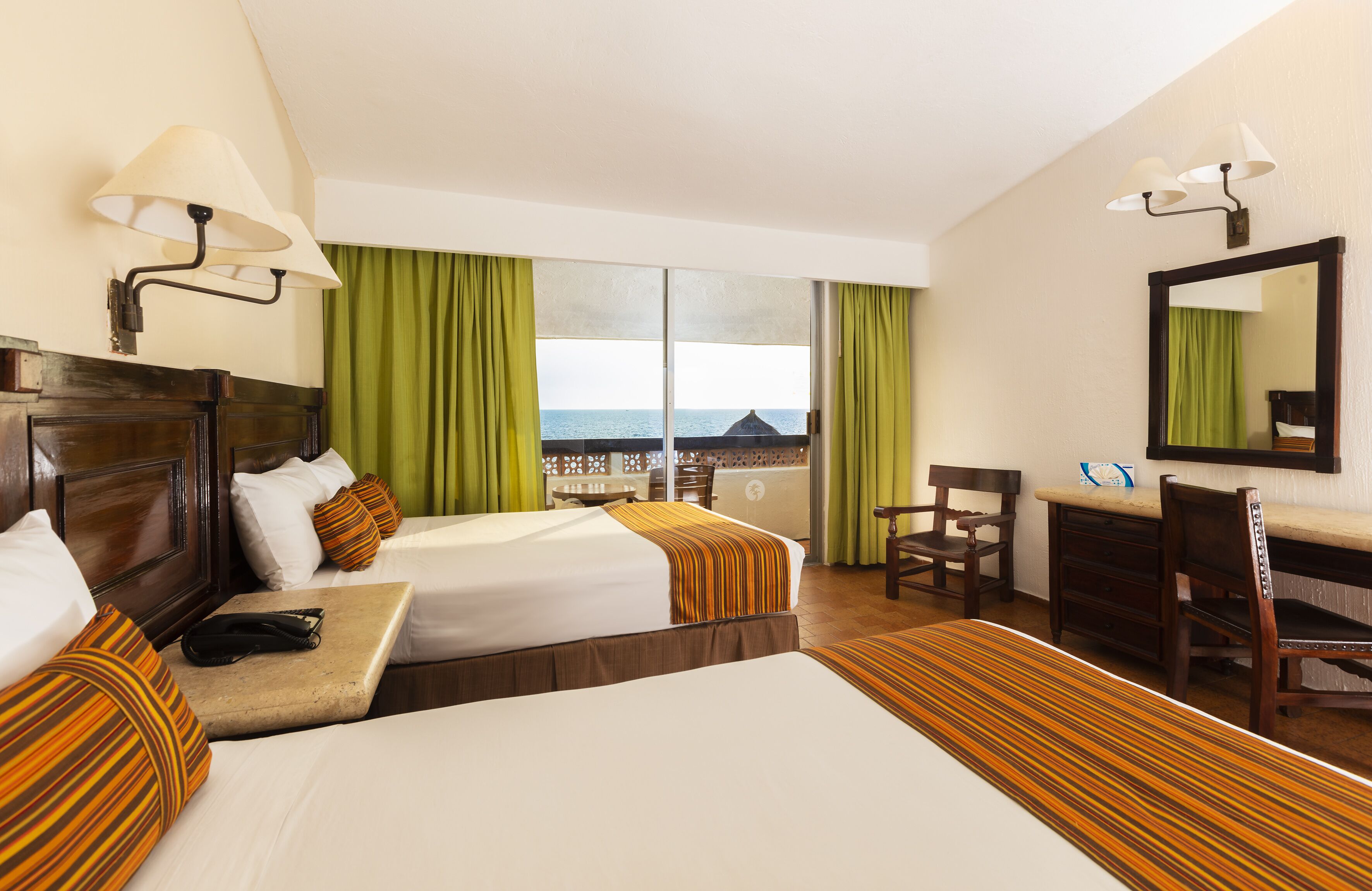 Ein Hotelzimmer mit zwei Betten, einem Schreibtisch, einem Stuhl, einem Spiegel und Meerblick.