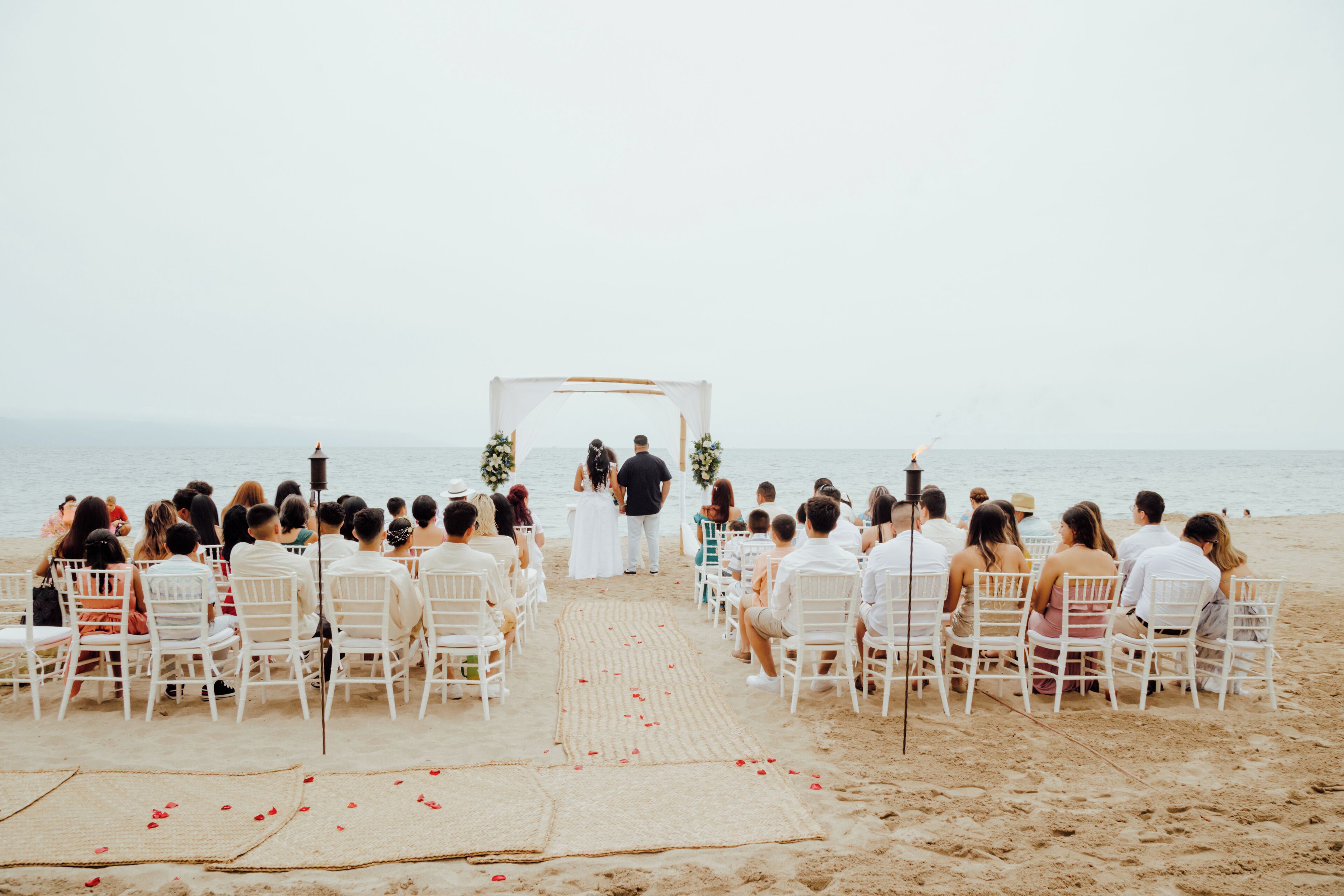 Ceremonia de boda en la playa, con sillas blancas dispuestas en filas mirando a la pareja en el altar.
