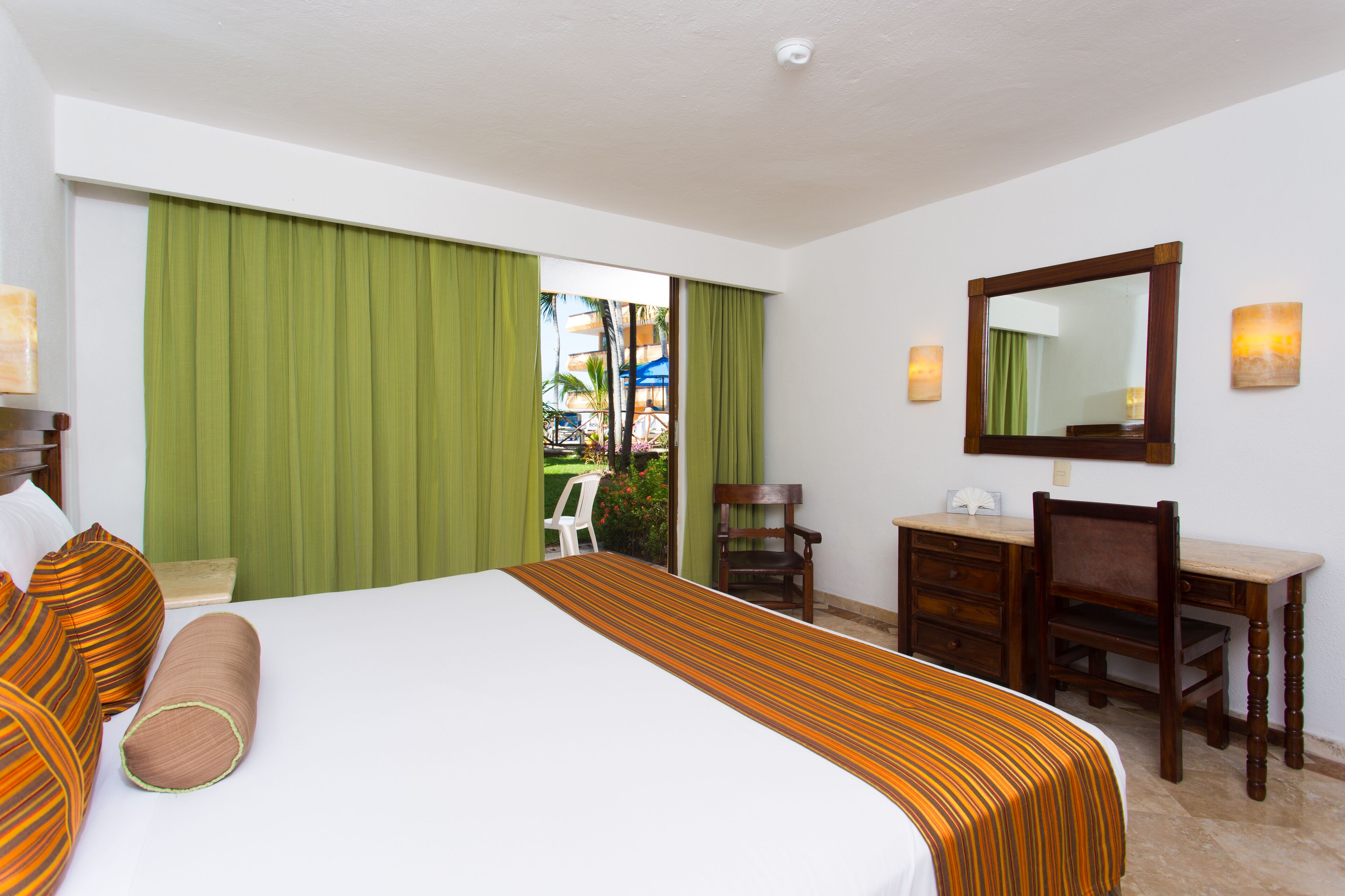 A hotel room with a bed, a desk, a chair, a mirror, and a view of the outside.