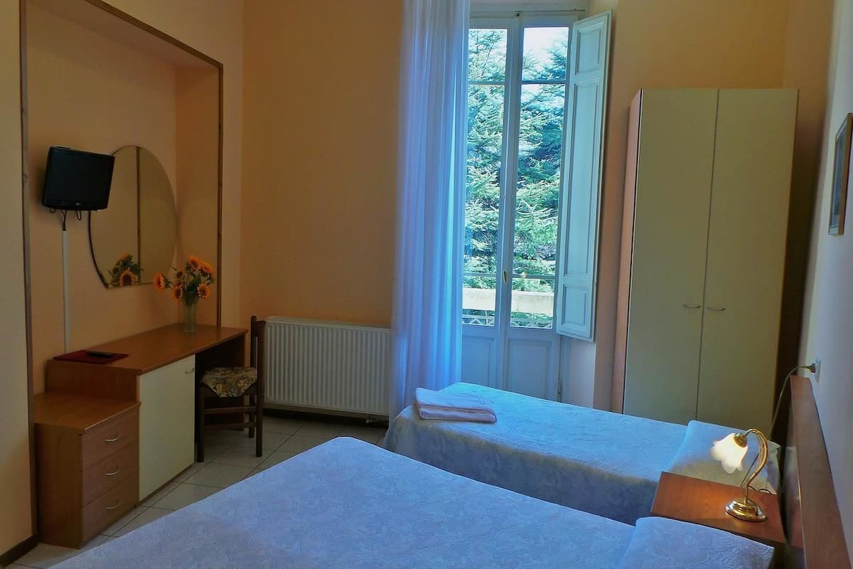 A bedroom with two beds, a desk, a chair, a TV, and a wardrobe.