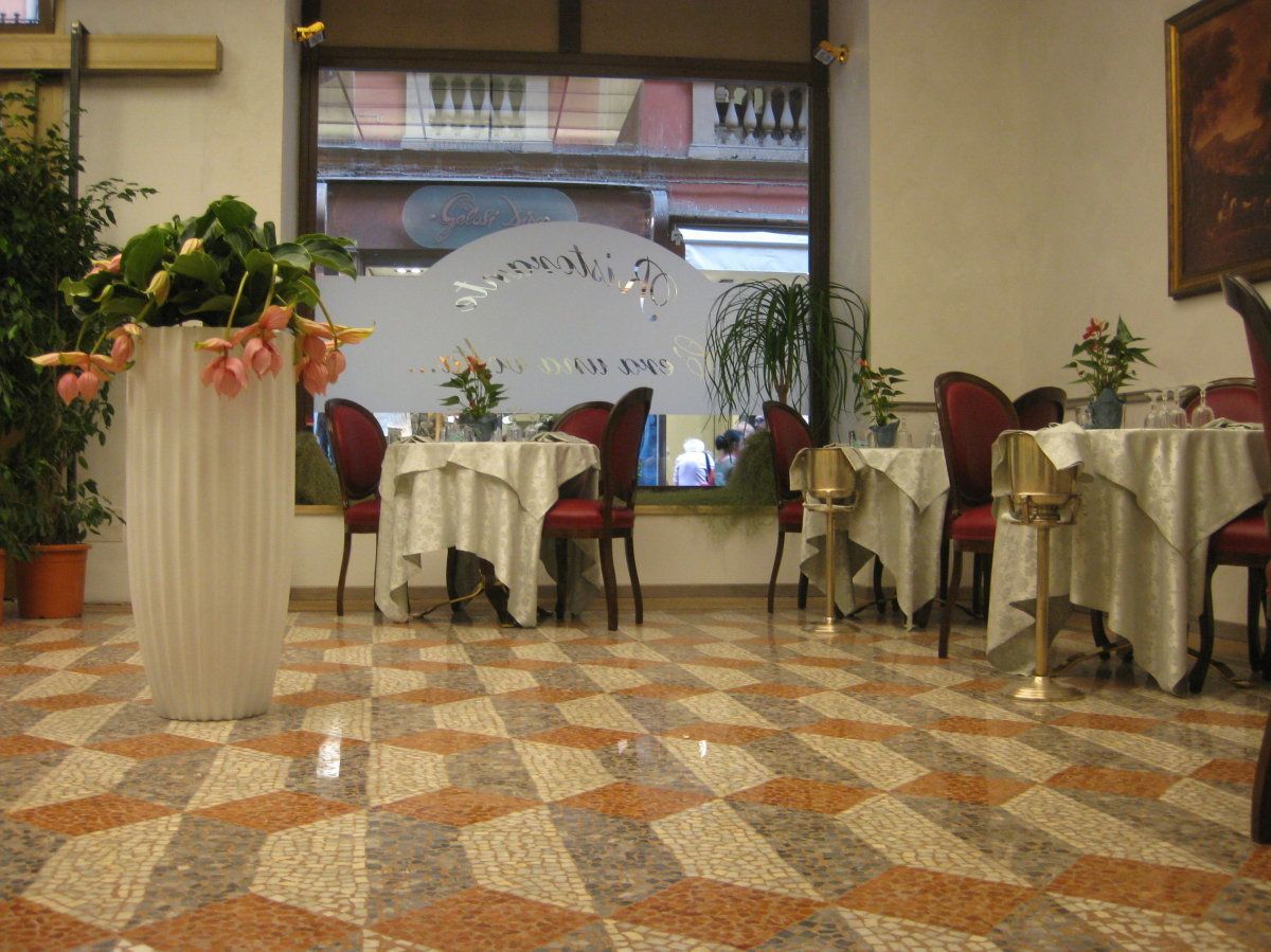 Zona pranzo con tavoli e sedie, una grande pianta in vaso e un pavimento decorato.