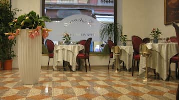 Zona pranzo con tavoli e sedie, una grande pianta in vaso e un pavimento decorato.