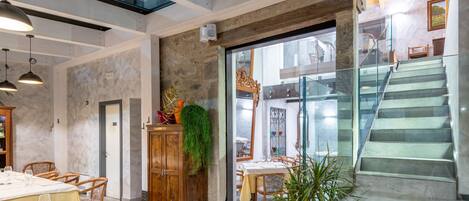 A dining area with tables set for service, a wooden cabinet with greenery, and a staircase leading to an upper level.