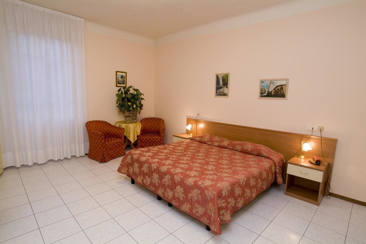 Habitación de hotel con cama, dos sillas, una mesita con una planta y dos lámparas de noche.
