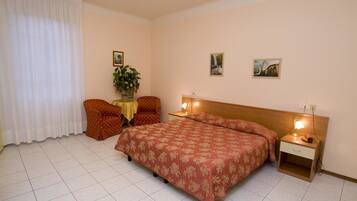 Habitación de hotel con cama, dos sillas, una mesita con una planta y dos lámparas de noche.