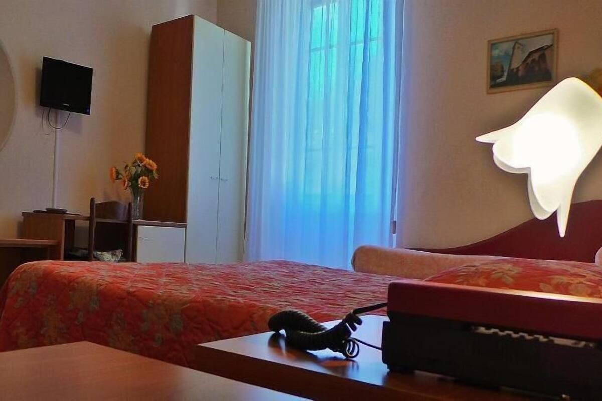 A hotel room with a bed, a desk, a chair, a TV, a wardrobe, and a window with curtains.
