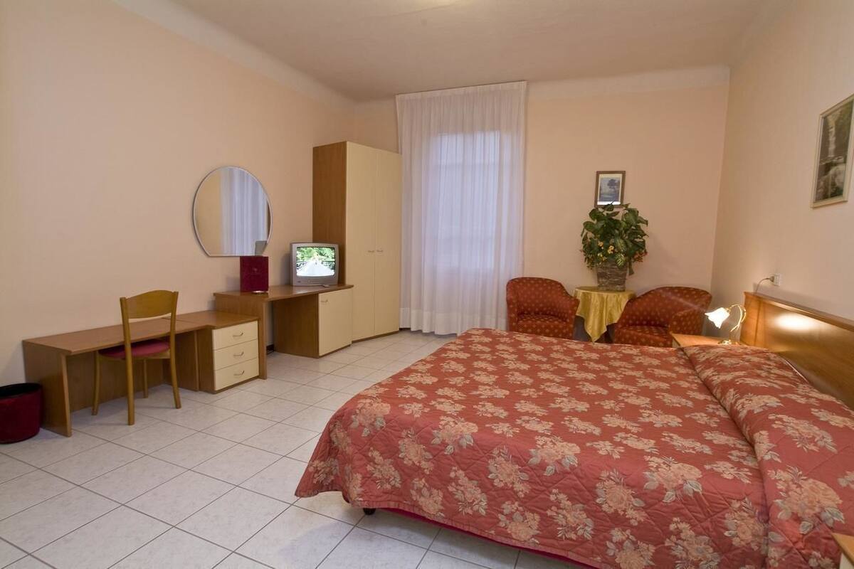 A bedroom with a bed, desk, chair, wardrobe, and a television.