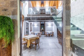 A modern dining area with wooden tables and chairs, a glass staircase, and a stone wall.