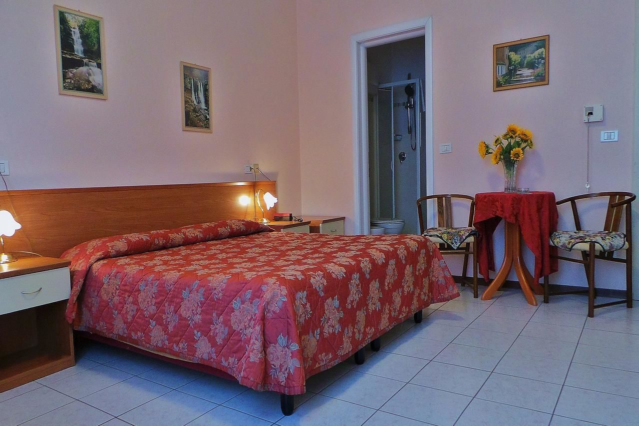 Ein Schlafzimmer mit einem Bett, Nachttischen, einem Beistelltisch, einem Sessel, einem Tisch mit roter Tischdecke und einer Vase mit Blumen.