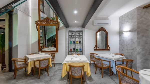 A dining area with tables set for four, wooden chairs with patterned upholstery, and ornate mirrors on the walls.