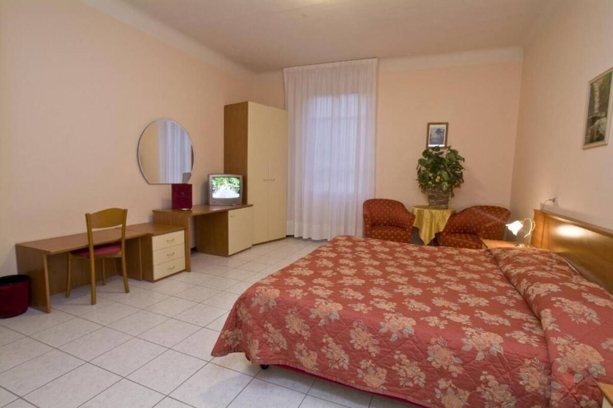 A bedroom with a bed, desk, chair, wardrobe, and a television.