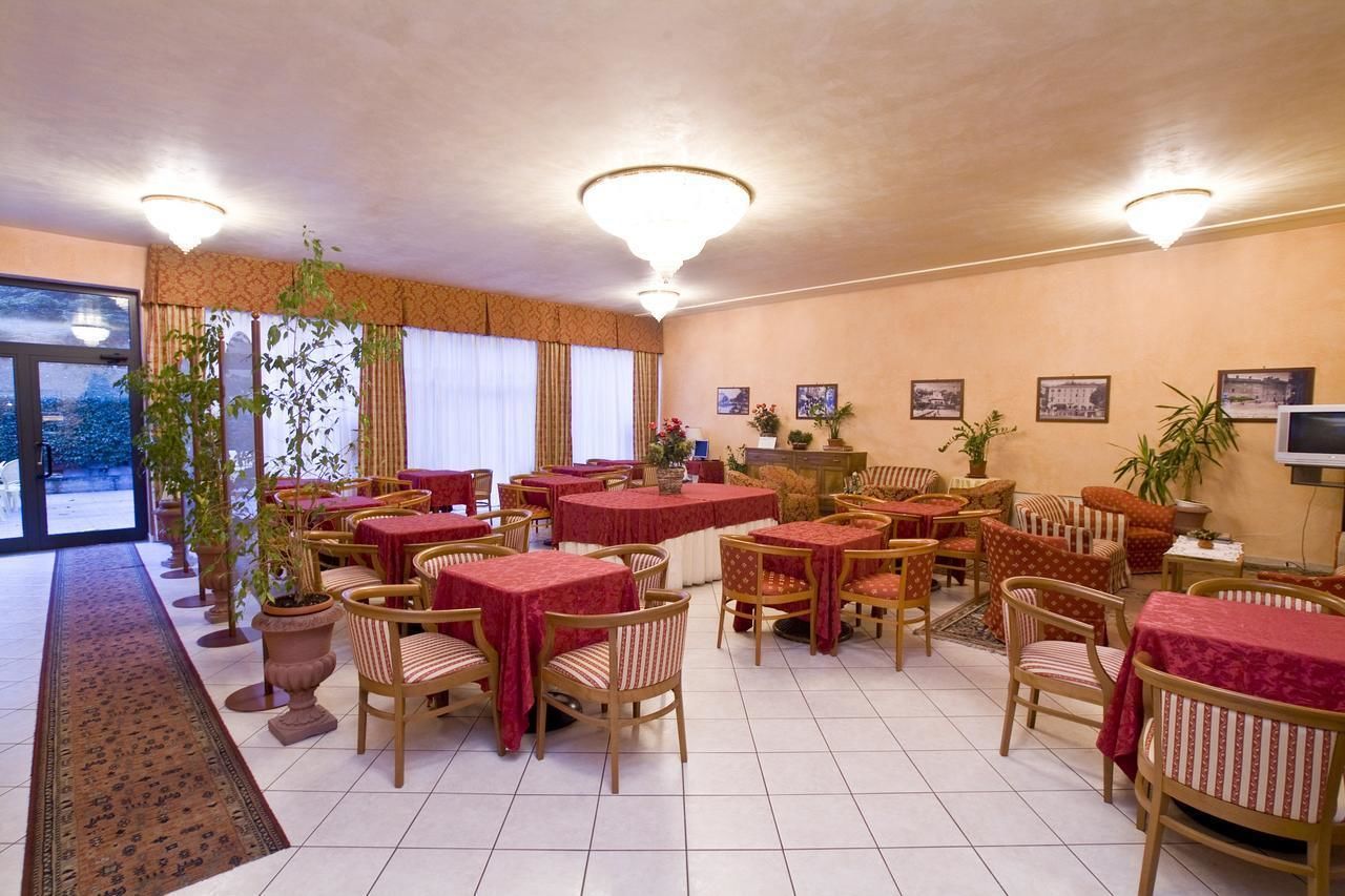 Ein Restaurant mit runden Tischen und Stühlen, Zimmerpflanzen und gerahmten Bildern an den Wänden.