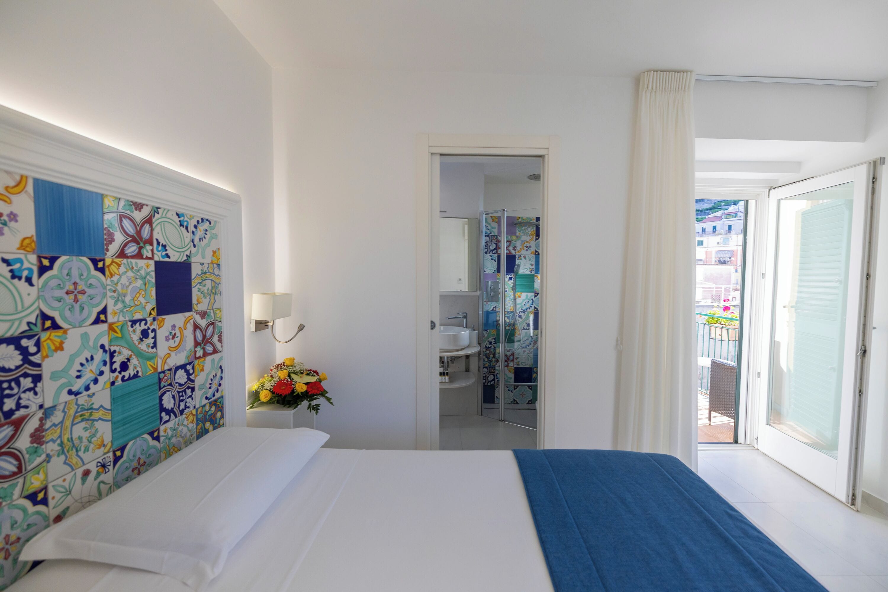 A hotel room with a bed, a bathroom with a shower, and a balcony with a view.