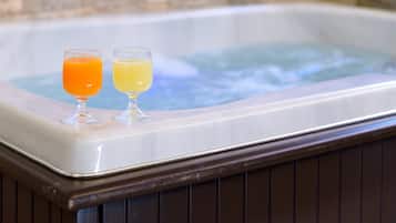 A hot tub with two glasses of beverages on its edge.