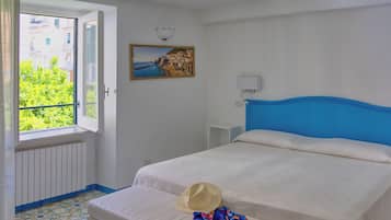 A bedroom with a bed, a window with a view of greenery, a painting on the wall, and a radiator.