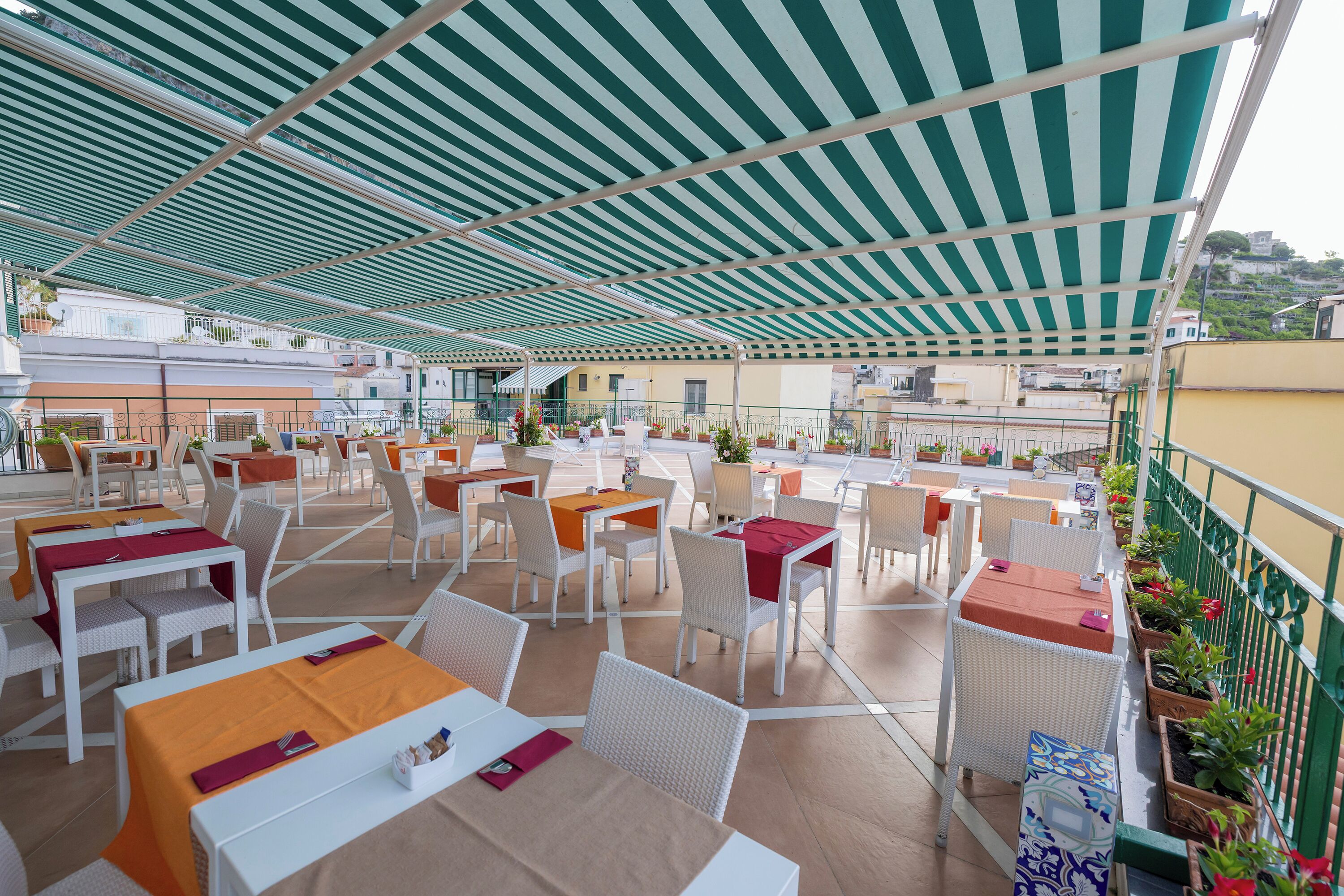 An outdoor dining area with tables and chairs, a striped awning, and potted plants.