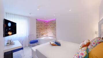 Una habitación de hotel moderna con una cama grande, un escritorio con computadora, televisión y un baño con pared de piedra y bañera.