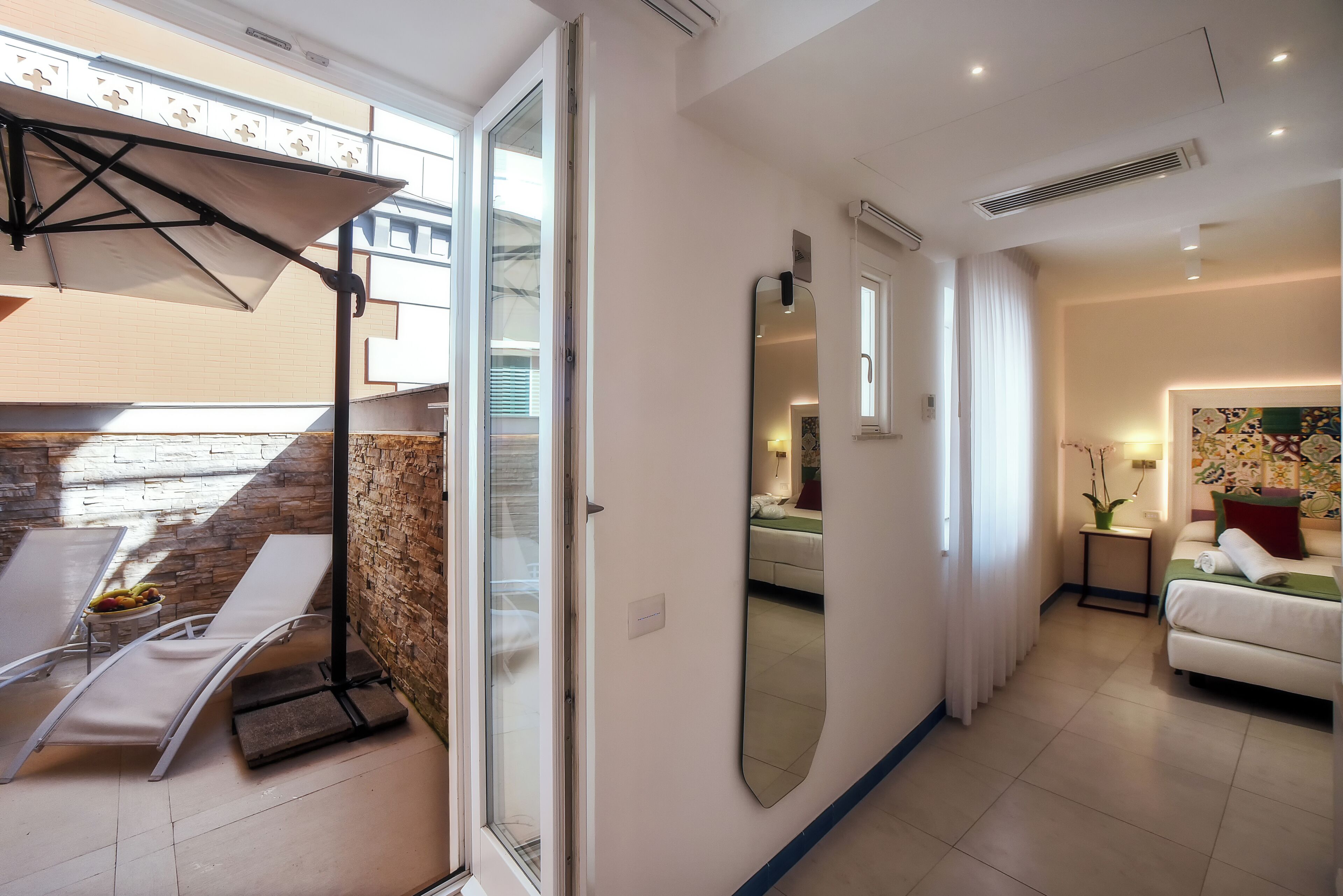 A modern hotel room with a balcony, a large mirror, a bed, and a small table with fruit.