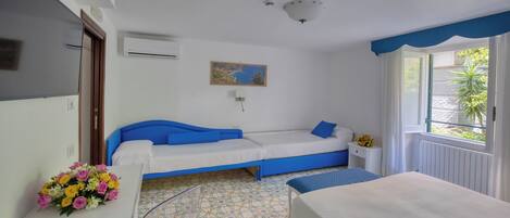 Una habitación con cama, un sofá, una mesita con un florero y una ventana con vistas a zonas verdes.
