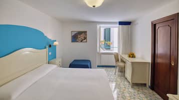 A hotel room with a bed, a desk, a chair, a window with curtains, a door, and a picture on the wall.