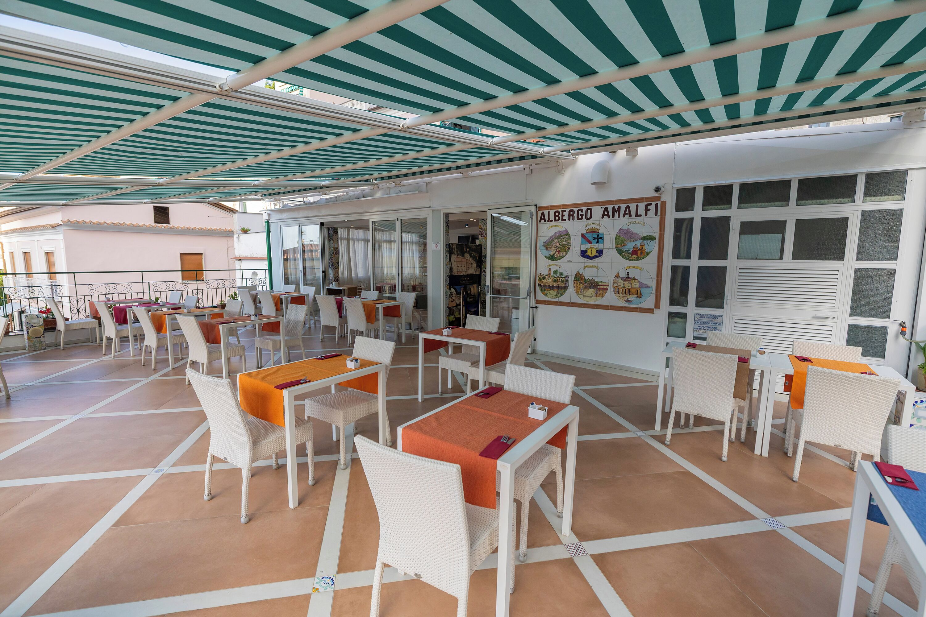 A covered outdoor dining area with white wicker furniture and orange tablecloths.