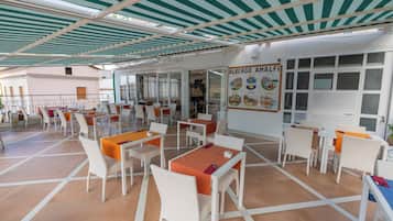 Un espacio de comedor al aire libre cubierto con mobiliario de mimbre blanco y manteles naranja.
