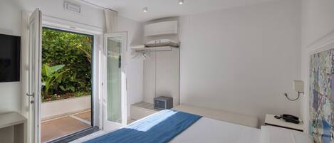 A bedroom with a bed, a bedside table with a phone, a wardrobe, and a door leading to a balcony.