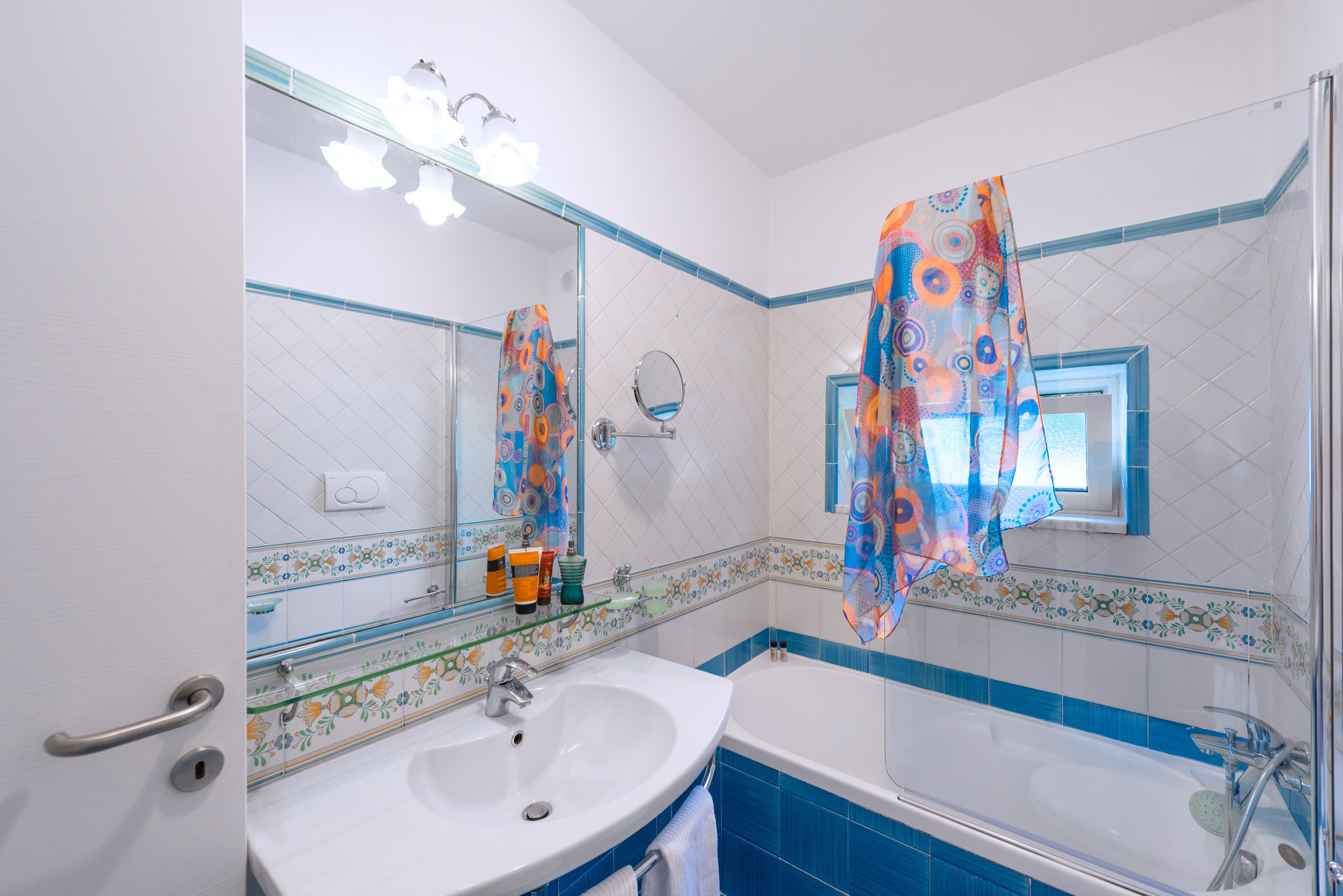 Un baño con lavamanos blanco, un espejo, una bañera y paredes con azulejos azules.