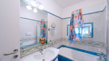 Un baño con lavamanos blanco, un espejo, una bañera y paredes con azulejos azules.