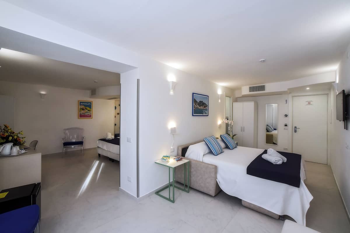 Une chambre d’hôtel comprenant un lit, une table de chevet, une chaise et un bureau avec une autre chaise.