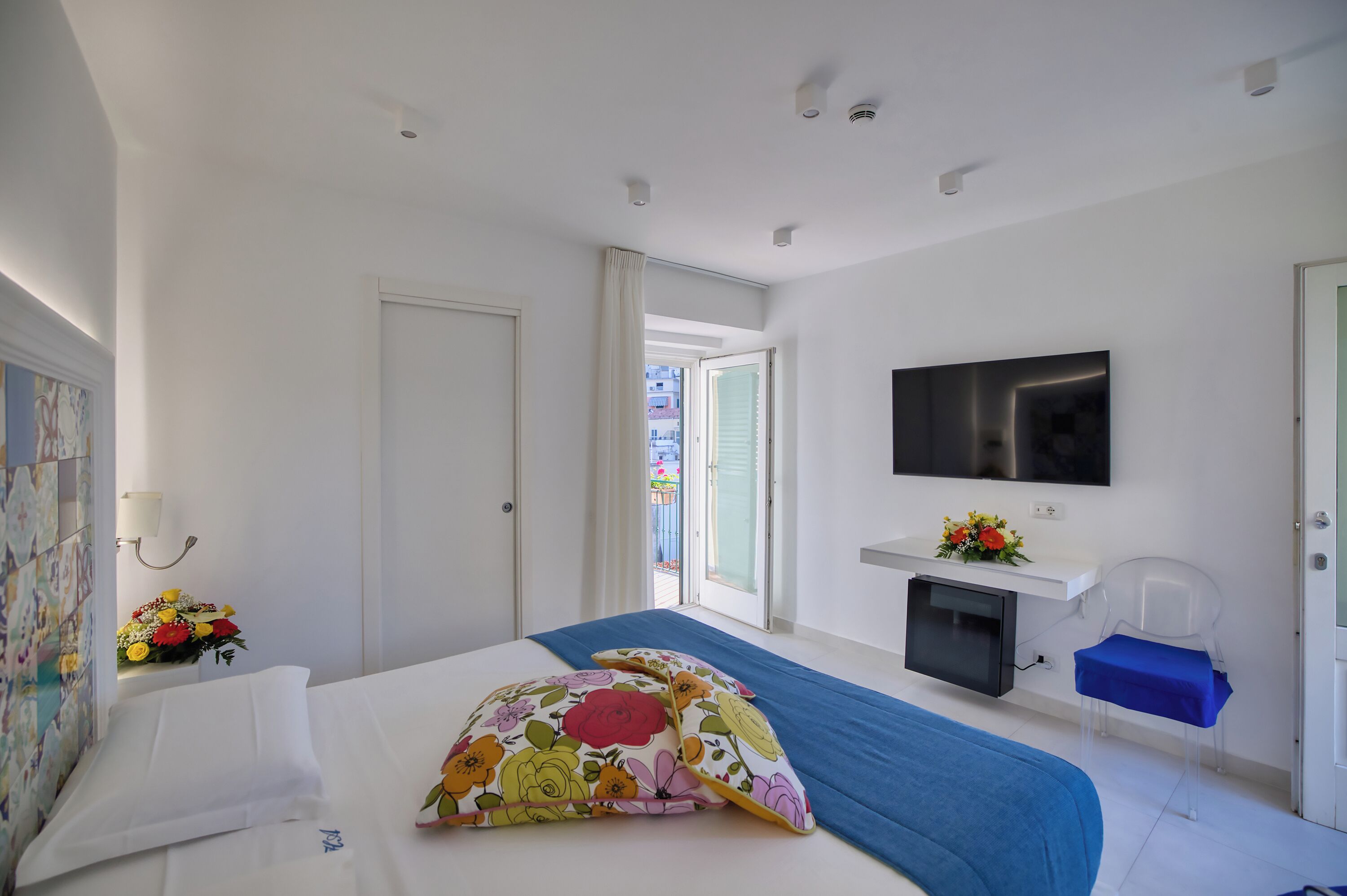 A hotel room with a bed, a TV, a small desk, and a window with an open door.