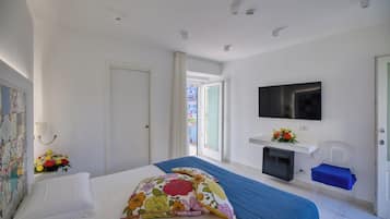 A hotel room with a bed, a TV, a small desk, and a window with an open door.