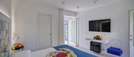 A hotel room with a bed, a TV, a small desk, and a window with an open door.
