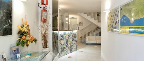 A modern hotel lobby with a glass reception desk, a staircase, and a large map on the wall.