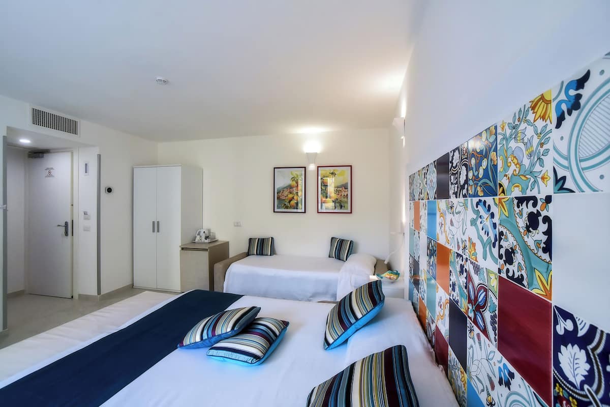 Une chambre d’hôtel avec deux lits, une armoire, un bureau et un mur recouvert de carreaux colorés.