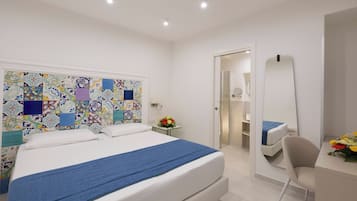 Une chambre à coucher avec un lit, un bureau, une chaise, un miroir et une salle de bain visible à travers une porte ouverte.