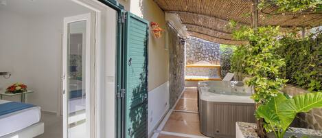 A hotel room with a sliding glass door, a small table with flowers, a hot tub, and a stone wall.