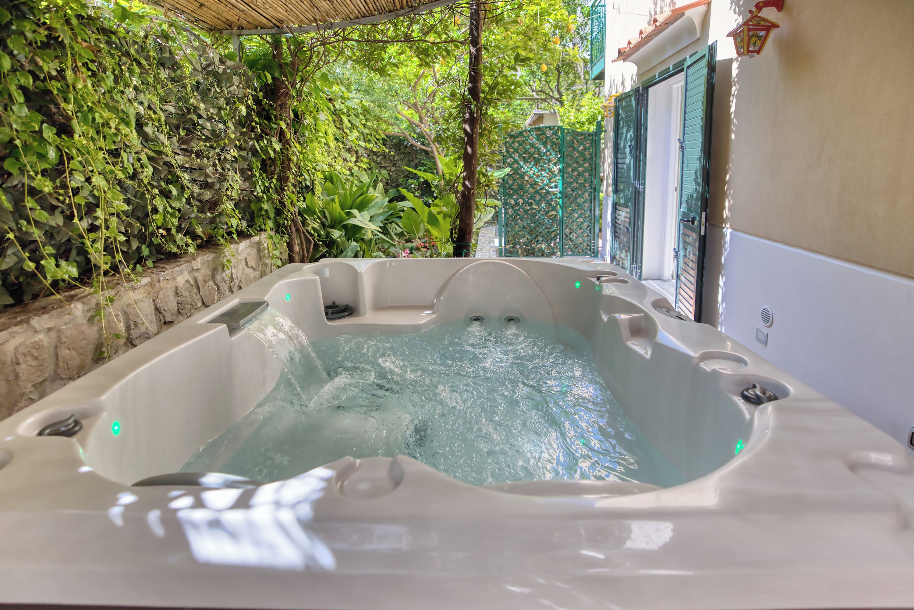 A hot tub in an outdoor setting with a stone wall and greenery.