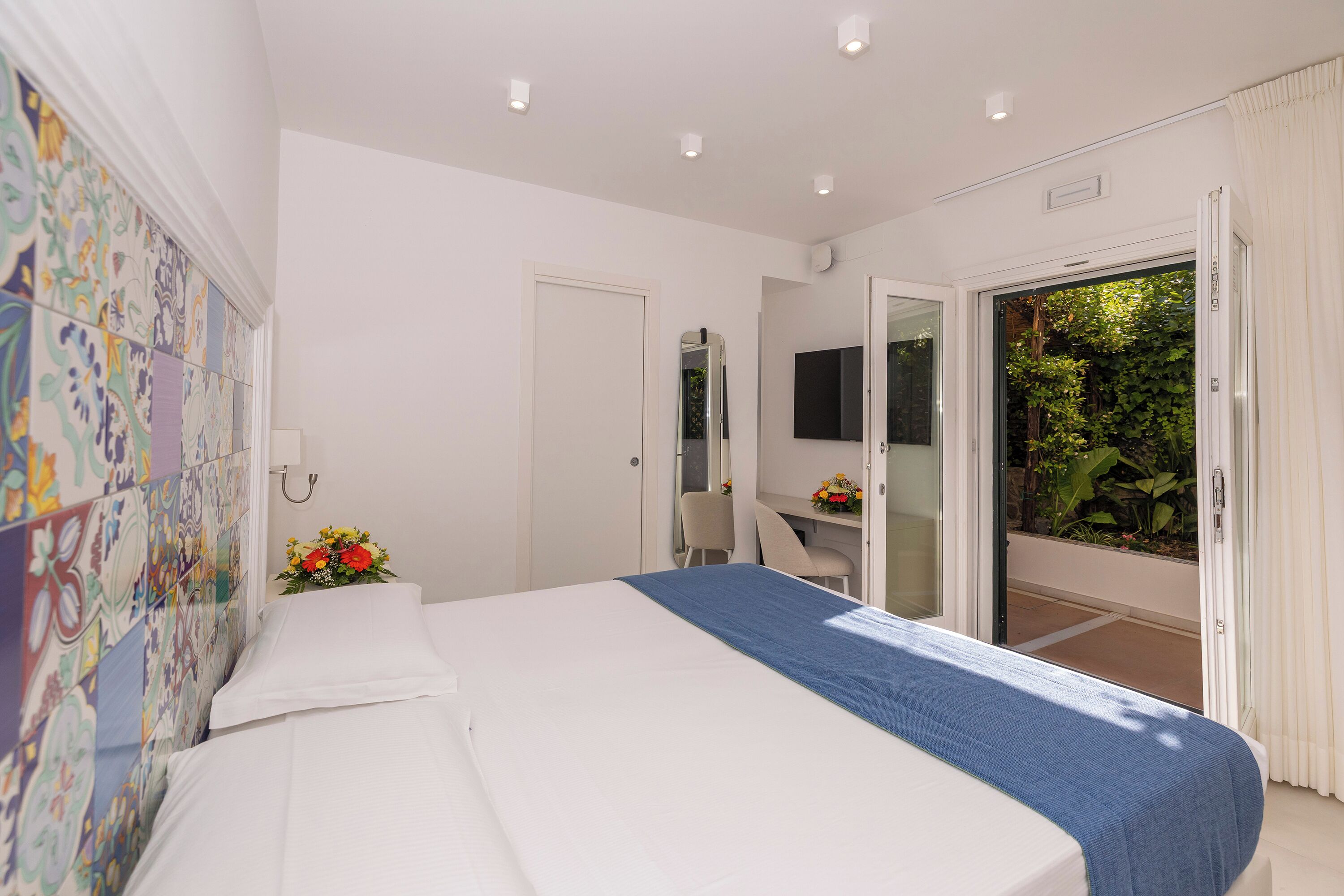Habitación de hotel con cama, escritorio, silla y vista a follaje a través de una puerta corrediza.