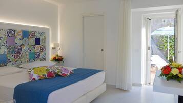 Une chambre à coucher avec un lit, une table de chevet, un mur orné d’un motif coloré, une porte et une vue sur l’extérieur.