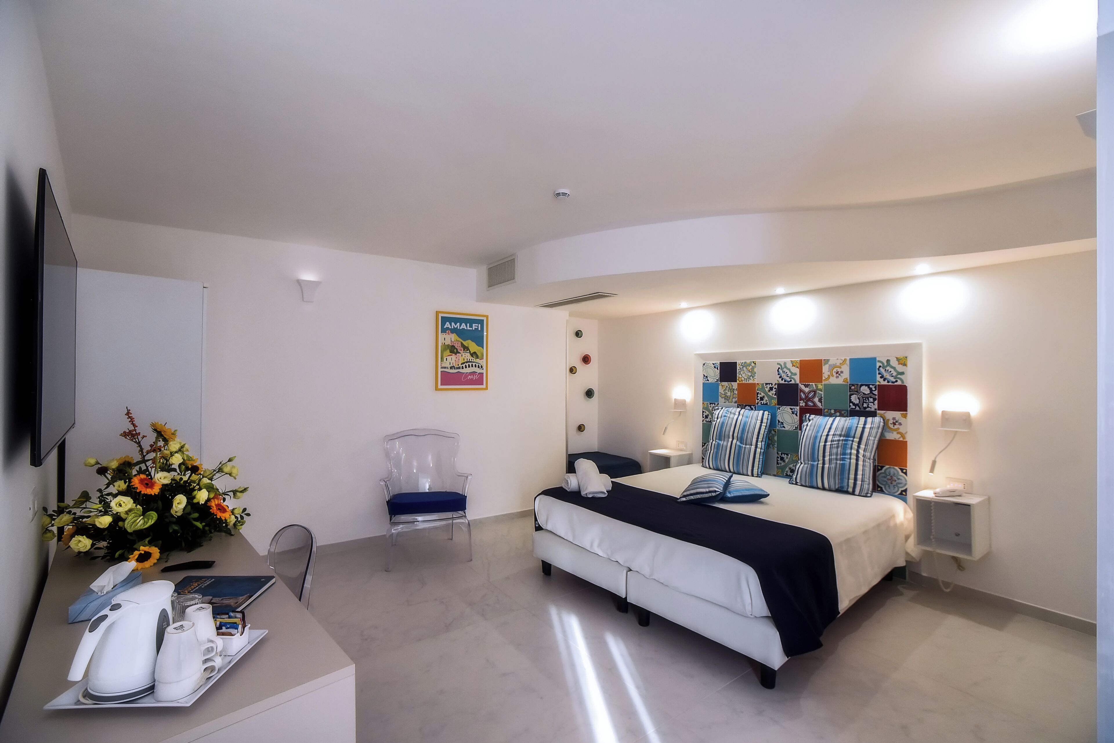 Ein Schlafzimmer mit Bett, Nachttischen, Schreibtisch mit Stuhl, Blumen in einer Vase und einem Poster an der Wand.