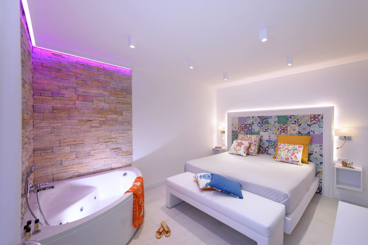 Une chambre à coucher moderne avec un grand lit, une baignoire intégrée et une tête de lit colorée.