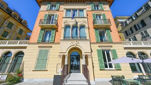 Un edificio histórico con una entrada central, contraventanas verdes y una bandera.