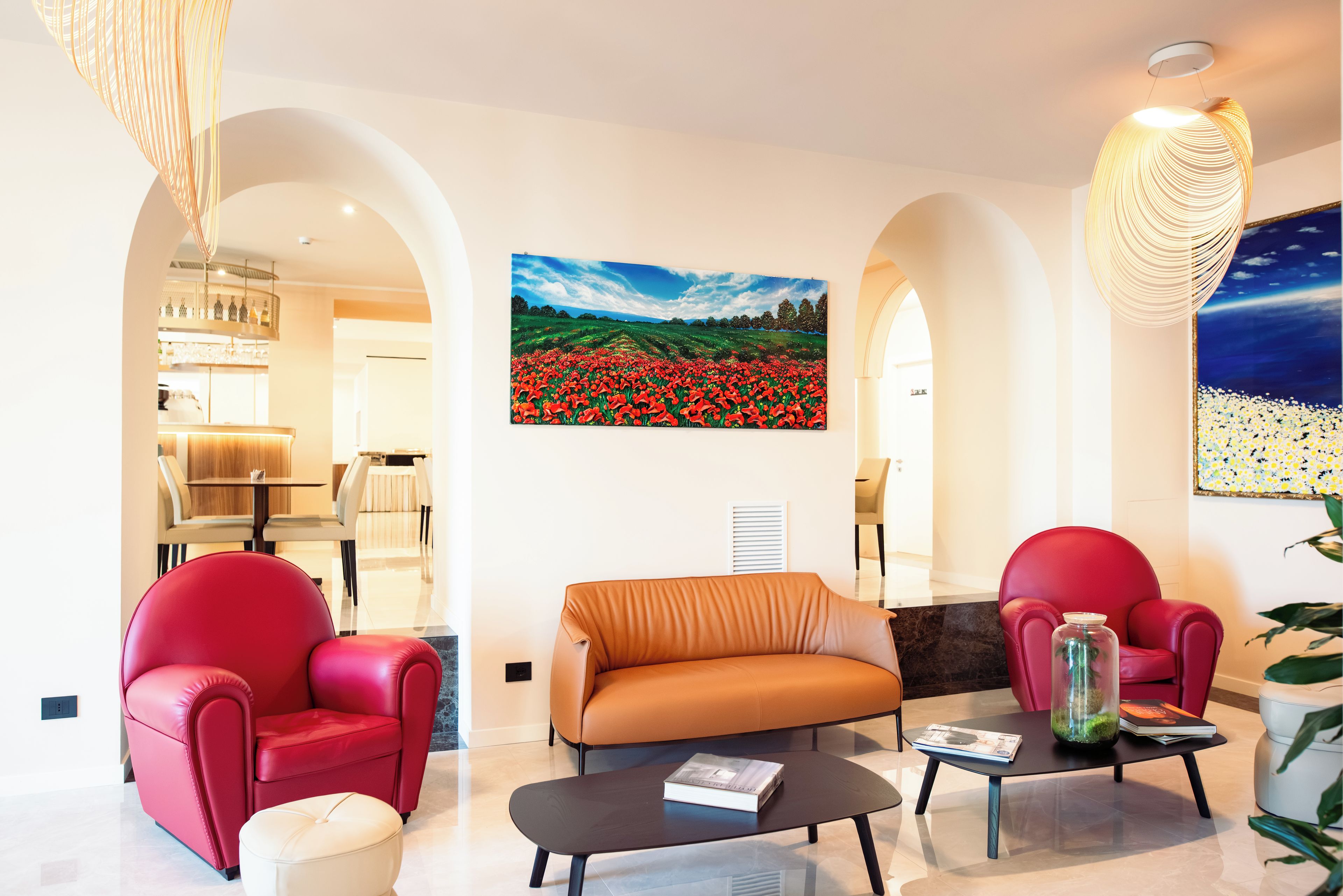 A modern living room with a sofa, two red chairs, a coffee table, and a painting of a field of red flowers on the wall.