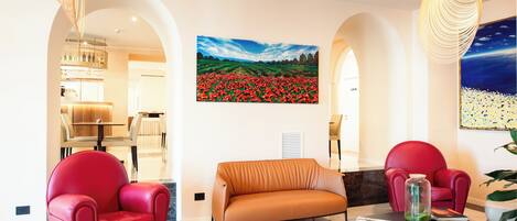 A modern living room with a sofa, two red chairs, a coffee table, and a painting of a field of red flowers on the wall.