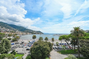 A coastal cityscape with a marina, parked cars, and lush greenery.