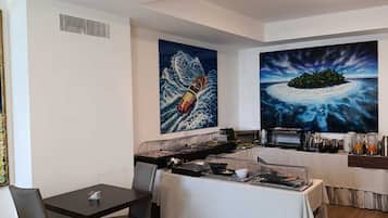 Un espace repas moderne avec une table dressée pour deux personnes, un buffet proposant divers plats et deux grandes peintures accrochées aux murs.