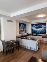 A modern dining area with a table set for two, a buffet with various food items, and two large paintings on the walls.