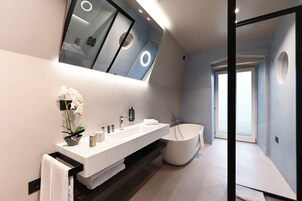 A modern bathroom with a large mirror, a white sink, a bathtub, and a potted orchid.